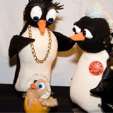 Zwei Plüschtier-Pinguine schauen auf ein gerade geschlüpftes Pinguingküken.