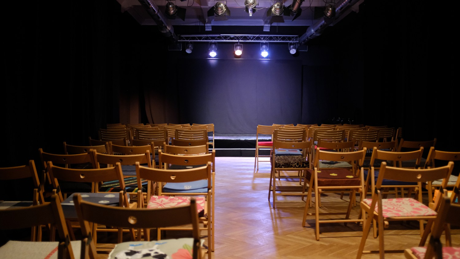 Foto mit Blick aus dem bestuhlten Saal zur Bühne im Scheinwerferlicht